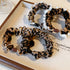 Product flat lay of leopard print scrunchies with white trim and decorative beads displayed on wooden tray against neutral background