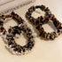 Three leopard print hair scrunchies arranged on decorative tray, featuring brown and black pattern with white trim and bead accents