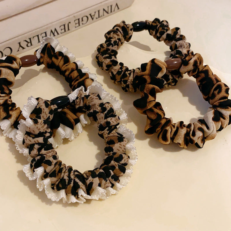 Three leopard print hair scrunchies arranged on decorative tray, featuring brown and black pattern with white trim and bead accents