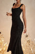 A model is holding a champagne glass wearing a black jacquard evening dress with ruched waist and fitted silhouette against champagne-colored background