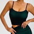 A woman is showcasing a dark green seamless crop top with thin straps and matching high-waisted compression leggings with piping detail