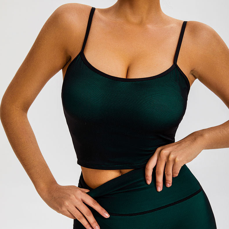 A woman is showcasing a dark green seamless crop top with thin straps and matching high-waisted compression leggings with piping detail