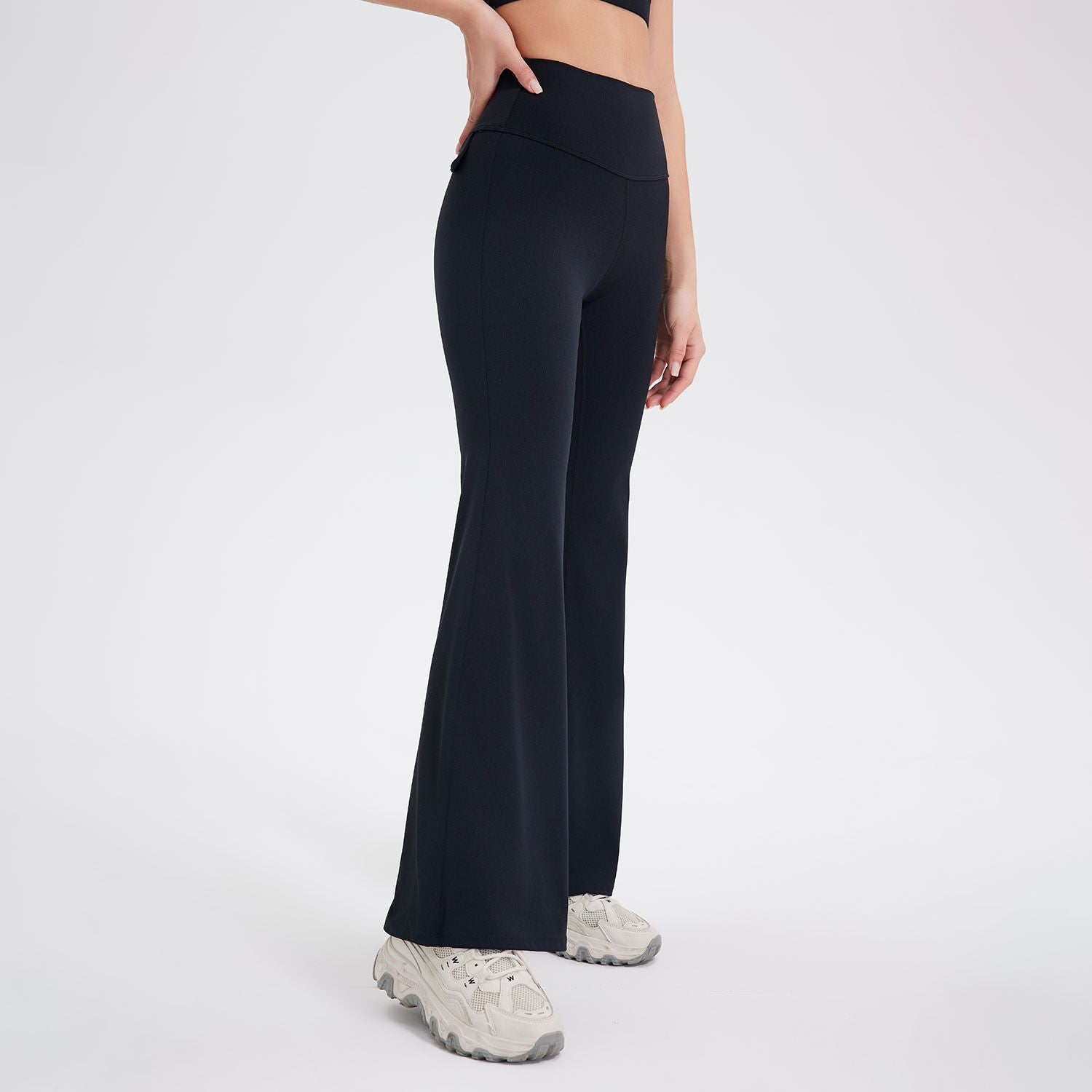 A side view of a person wearing black flared yoga pants with a high waistband, paired with a black sports bra and white platform sneakers