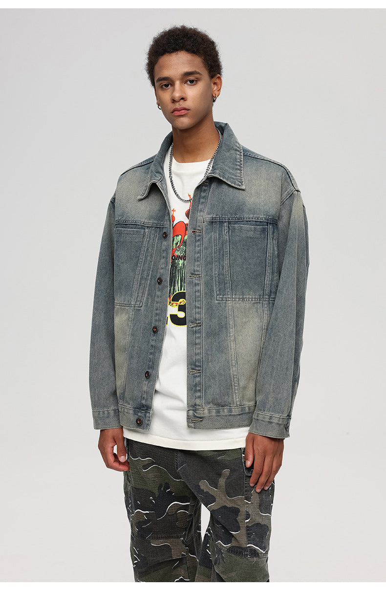 A man is posing at a slight angle against a gray background. Wearing vintage-wash denim jacket, white graphic tee and camouflage cargo pants