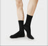 Model standing wearing black ribbed crew sports socks, showing full foot profile against minimalist white background