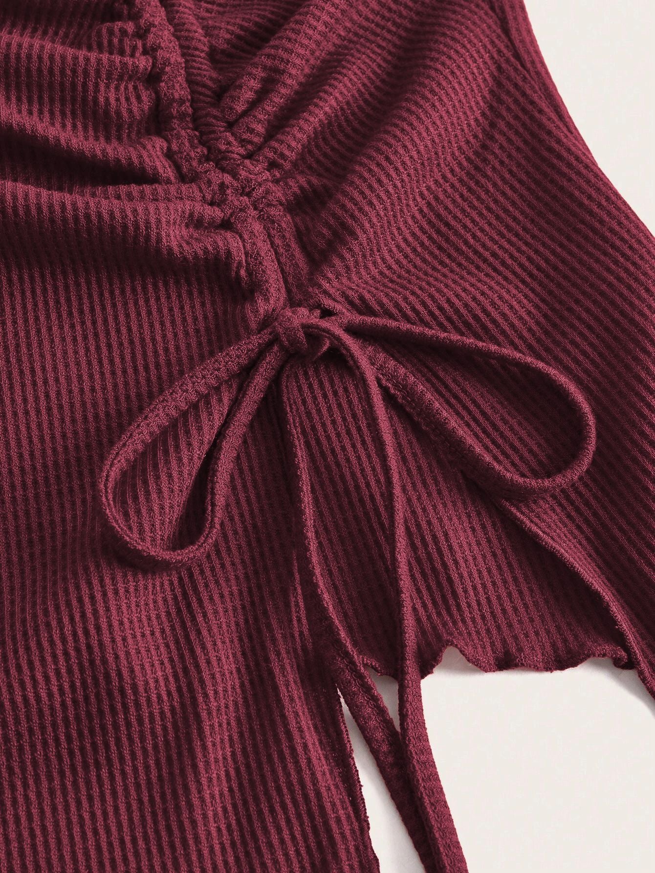 A detailed view of burgundy ribbed fabric showing adjustable drawstring design with bow tie feature and scalloped edge