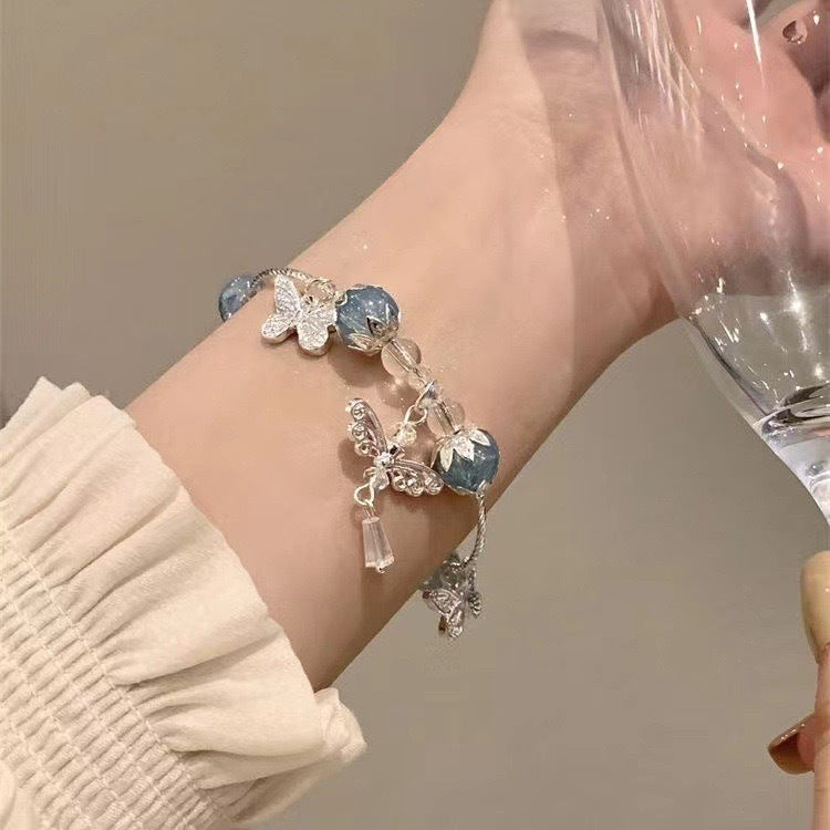 A woman wearing a delicate blue crystal and silver butterfly bracelet with cream sleeve details against a neutral background