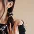 Side view of woman with ponytail wearing leopard print scrunchie, touching her hair while wearing black top with animal print detail