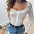 A woman wearing a striped long-sleeve bodysuit with a scoop neckline and button-up front, paired with distressed denim jeans and a black belt.