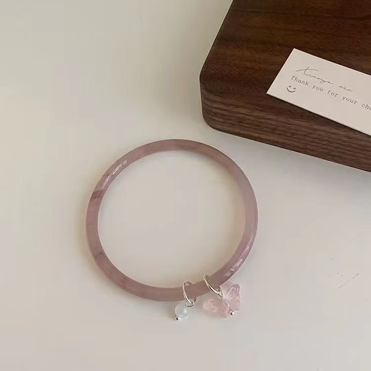 A delicate lavender jade bangle with small crystal and butterfly charms on white surface with wooden gift box