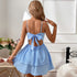 Back view of a woman in a light blue tiered mini dress with an open back and bow detail, posing in a bright room with floral decor