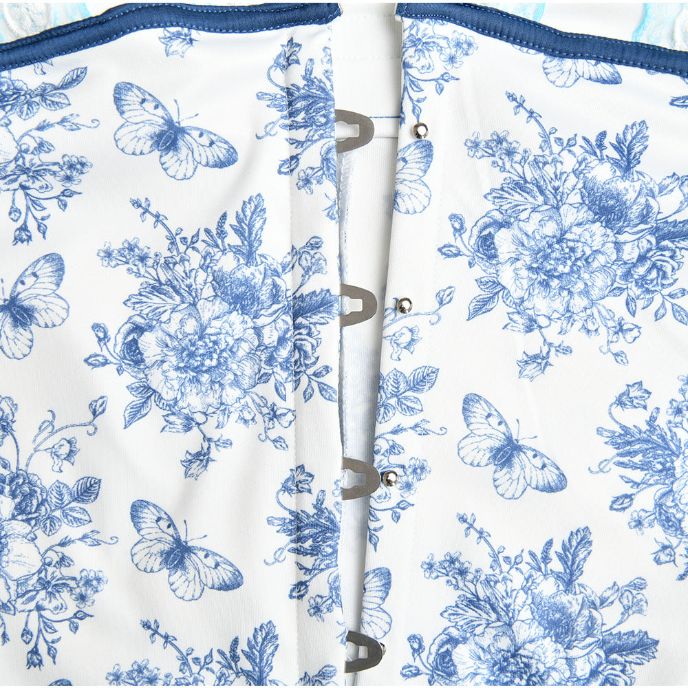 Close-up detail of a white and blue toile-print dress showing hook and eye closures with navy trim along the seam against white background