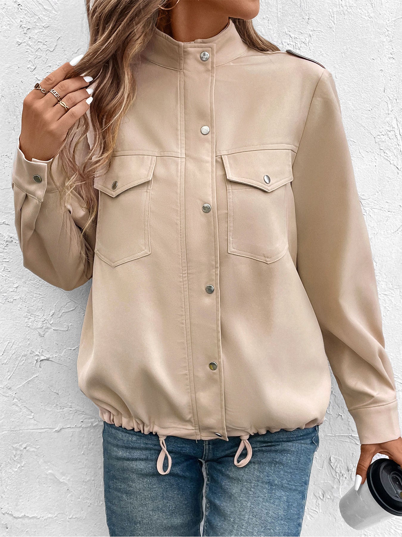 Women's beige utility jacket with front pockets and button details, styled casually with crop top