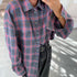 Purple and gray plaid flannel shirt with black jeans and gold bracelet