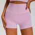 Model wearing high-waisted lavender workout shorts with seamless construction and white contrast stitching against white background