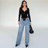 Full view of woman wearing a black tie-front bodysuit styled with wide-leg jeans, accessorized with pointed heels and a structured handbag.