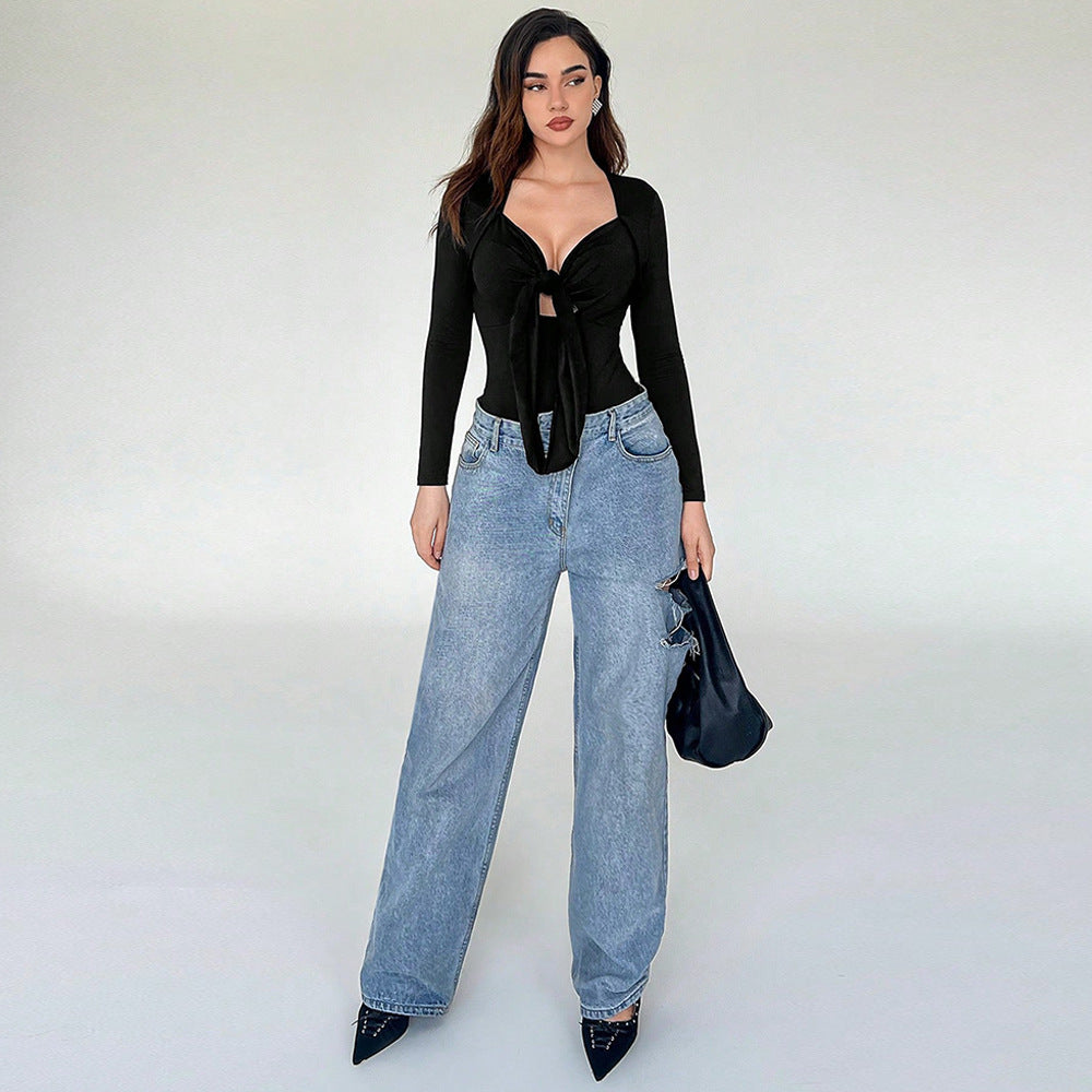 Full view of woman wearing a black tie-front bodysuit styled with wide-leg jeans, accessorized with pointed heels and a structured handbag.