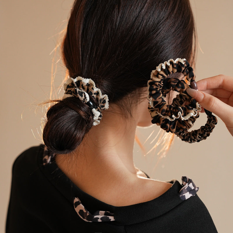 Back view of woman with low bun wearing leopard print scrunchie, holding another scrunchie in hand against neutral background