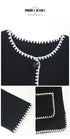 Close-up details of black cardigan showing decorative white contrast stitching and button closure