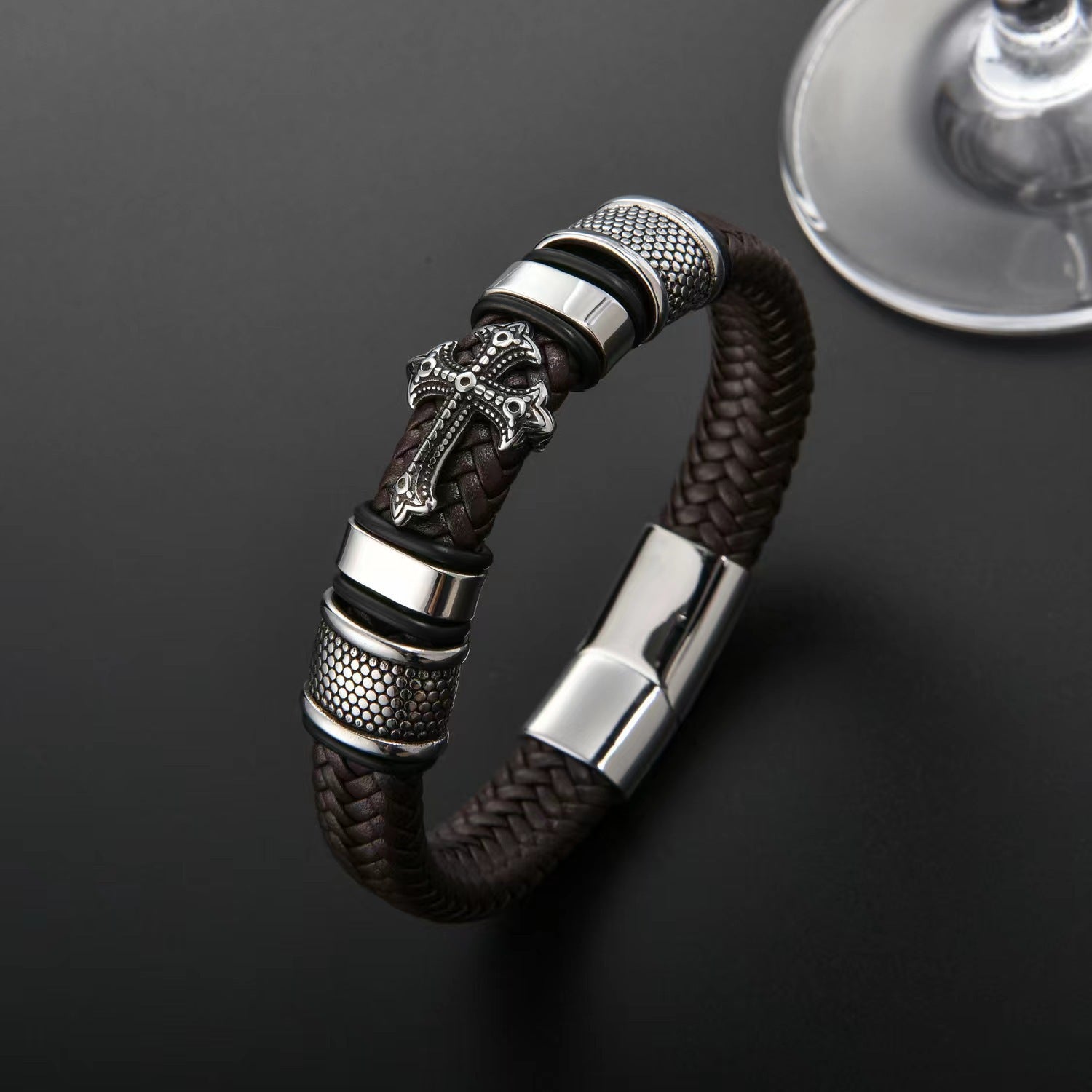 Close-up of a black braided leather bracelet with a gold-tone cross and detailed metal accents.