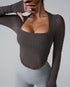 A woman wearing brown textured square-neck long sleeve top paired with light gray high-waisted leggings, hand touching face