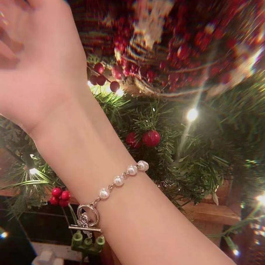 A pearl bracelet with silver toggle clasp worn on wrist against Christmas tree background with red ornaments and lights