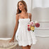 Woman wearing a white tiered mini dress with thin straps, holding a bouquet of pastel roses in an elegant indoor setting