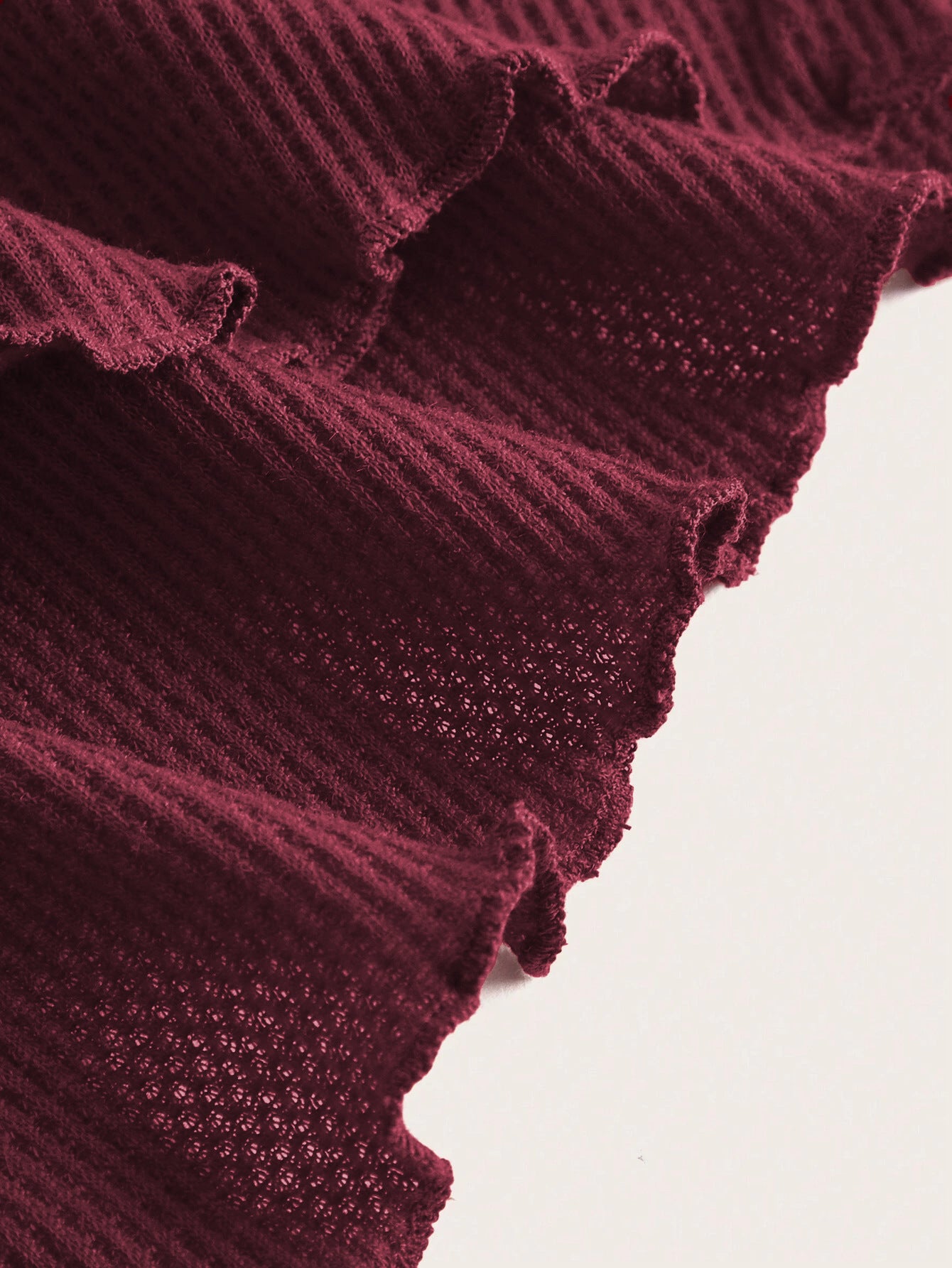 A close-up detail shot of burgundy ribbed fabric with lettuce edge trim and mesh panels showing garment construction