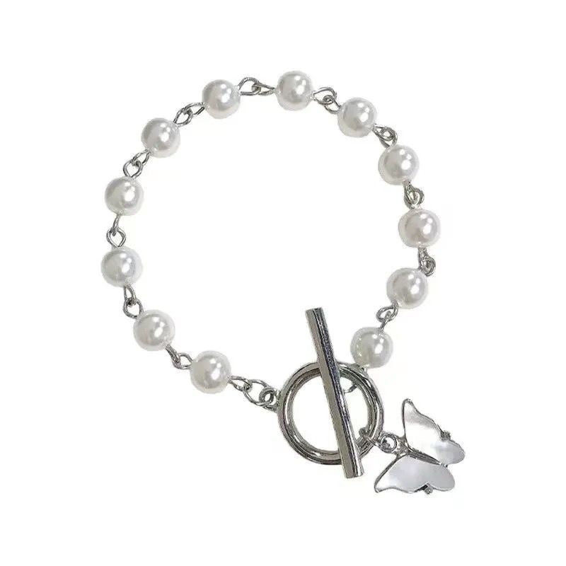 A white pearl bracelet with silver chain links, toggle clasp and butterfly charm photographed against white background