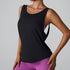 A woman is wearing a black sleeveless tank top with a scoop neckline over a pink sports bra, paired with purple leggings, posing against a neutral backdrop