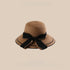 A khaki woven straw sun hat with a wide brim and a large black bow tied at the back, displayed against a beige background.