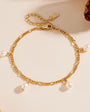 Gold chain bracelet with five teardrop pearl charms, laid flat on a beige surface.