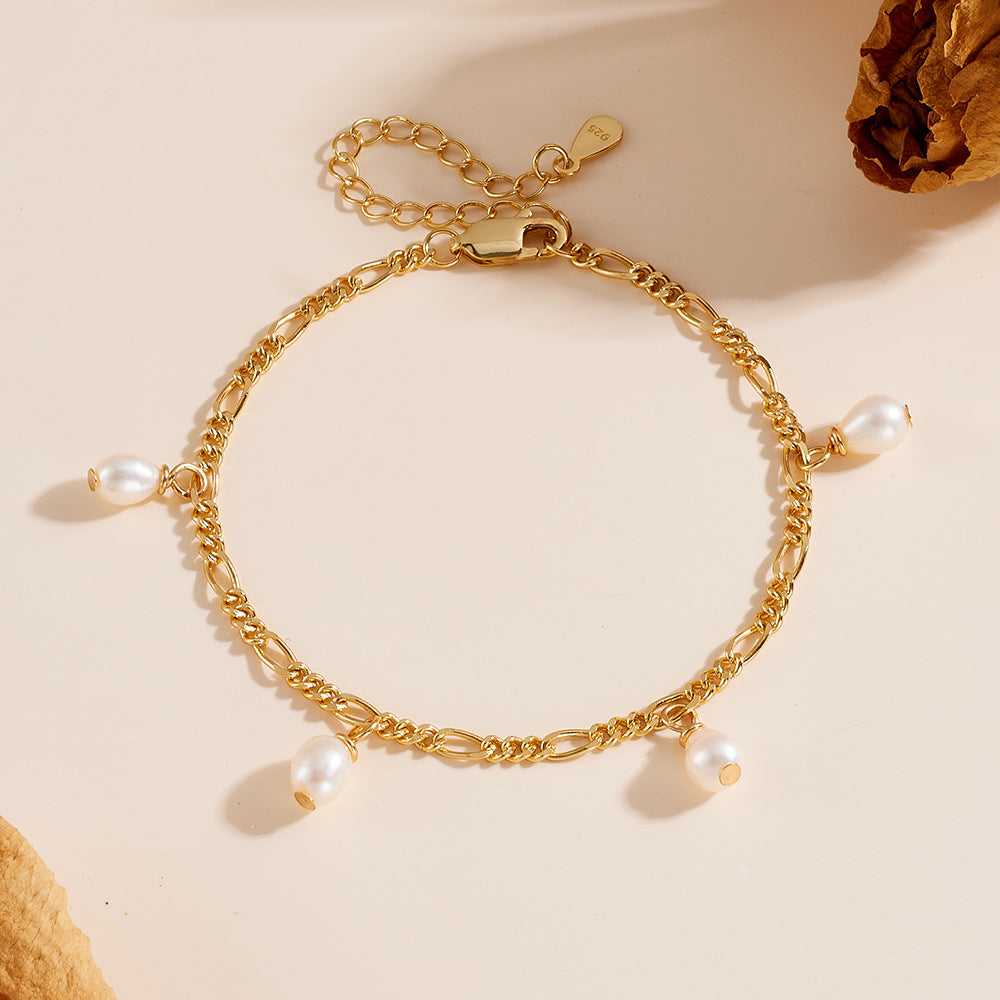 Gold chain bracelet with five teardrop pearl charms, laid flat on a beige surface.