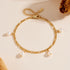 Gold chain bracelet with five teardrop pearl charms, laid flat on a beige surface.