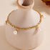 Gold pearl drop bracelet wrapped around a ceramic vase for display.