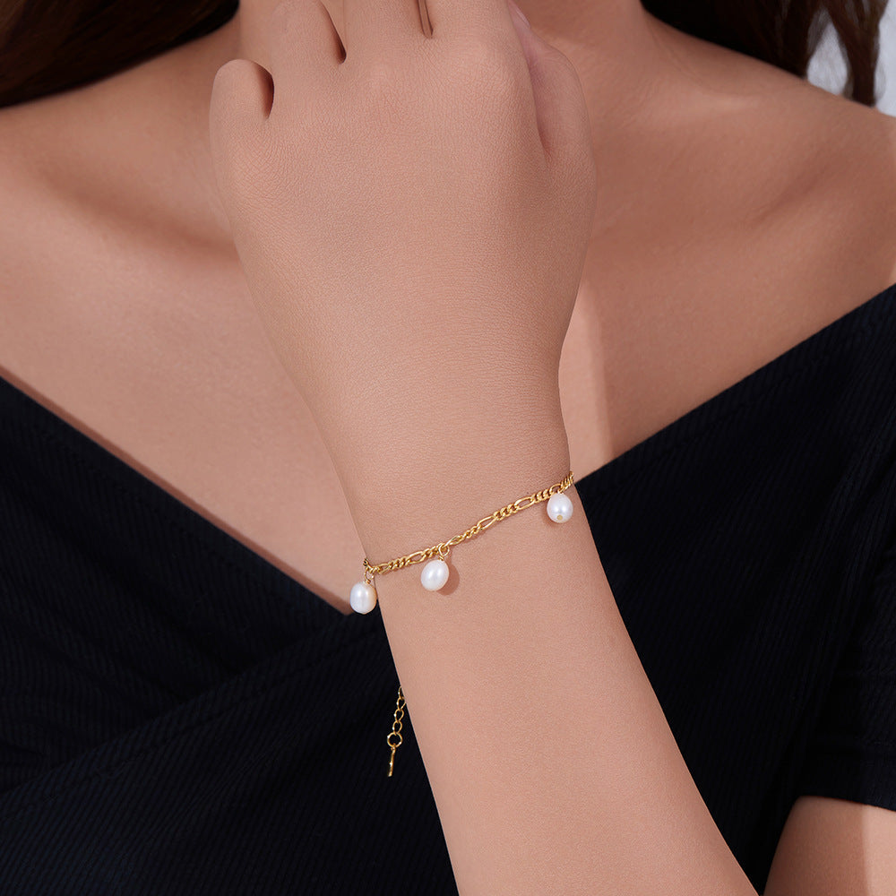Model wearing a gold bracelet with pearl drops, styled with an off-shoulder black top.