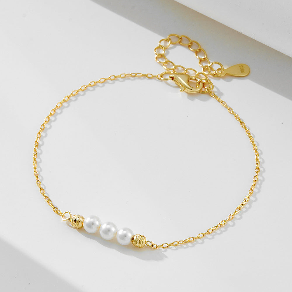 Gold chain bracelet with three white pearls and two textured gold beads.