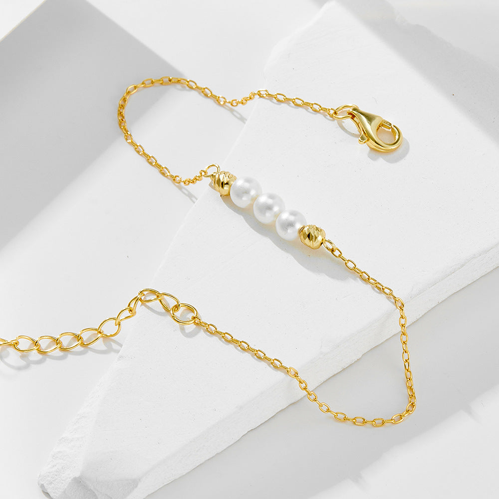 Delicate gold bracelet with pearls and gold beads resting on white geometric display.
