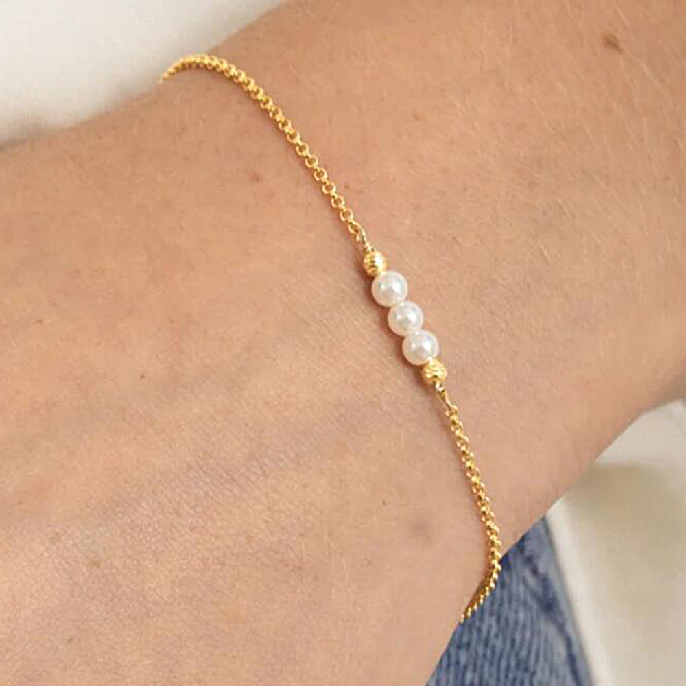 Close-up of gold bracelet with three white pearls and textured gold beads on wrist.