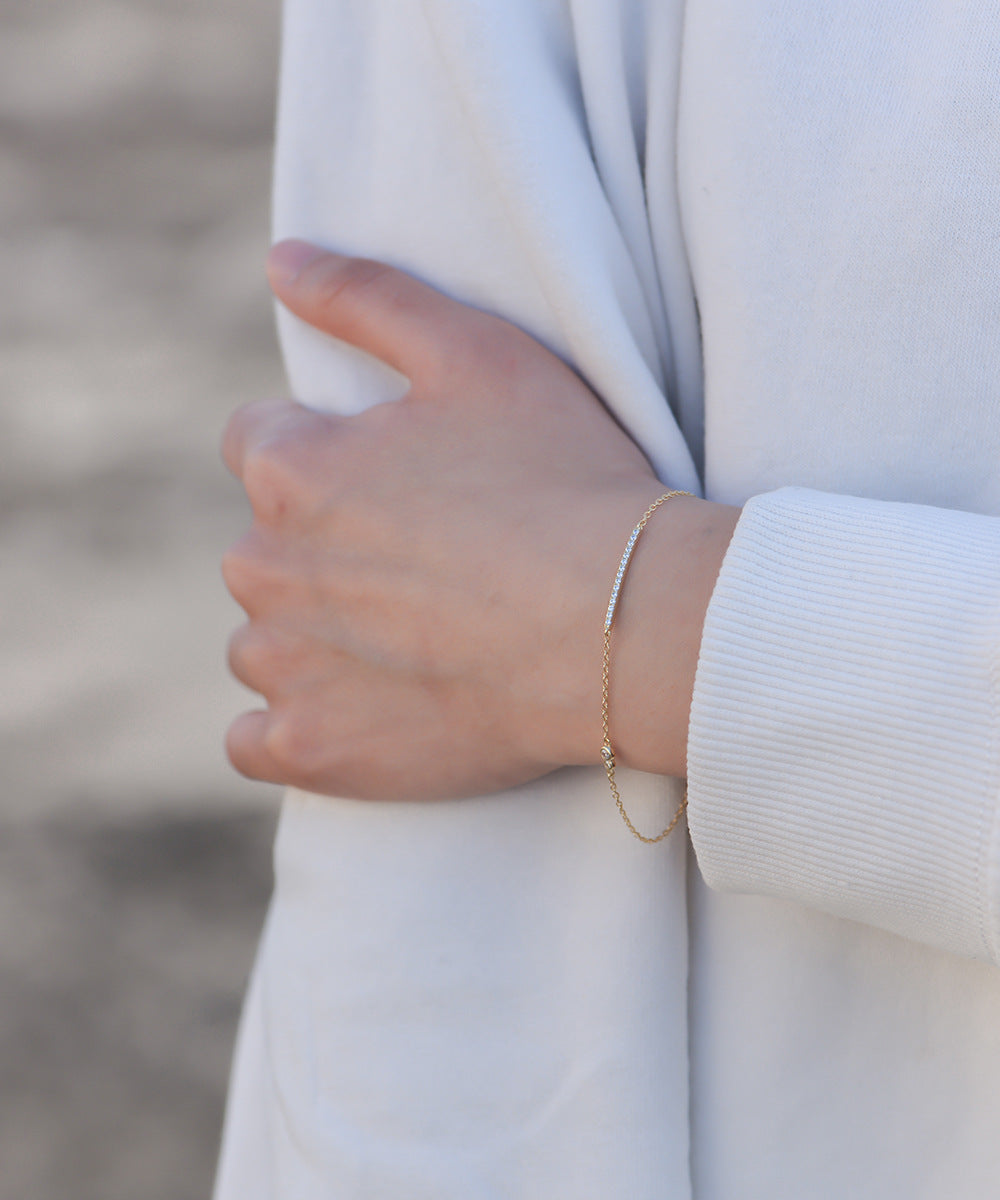 Full arm shot of gold bar bracelet styled with a white long sleeve.