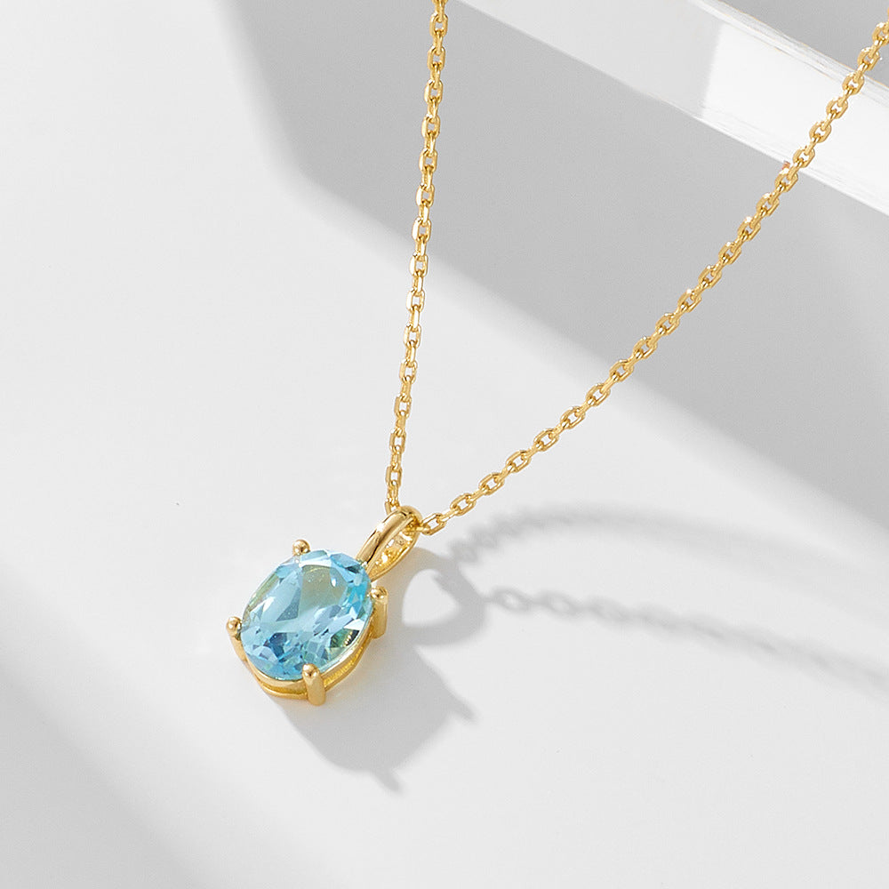 Angular view of gold-plated S925 necklace with oval-cut blue topaz pendant under soft light.