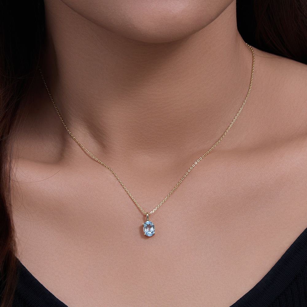 Woman wears gold S925 blue topaz pendant necklace against bare neckline.
