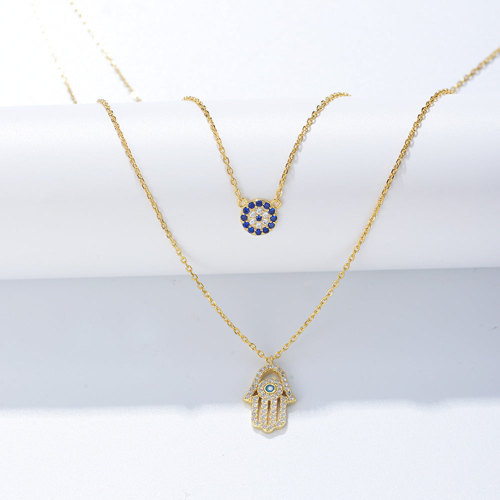Gold double-layer necklace with blue evil eye charm and crystal Hamsa pendant