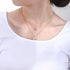 Model wears gold layered necklace with evil eye and Hamsa charms on white top