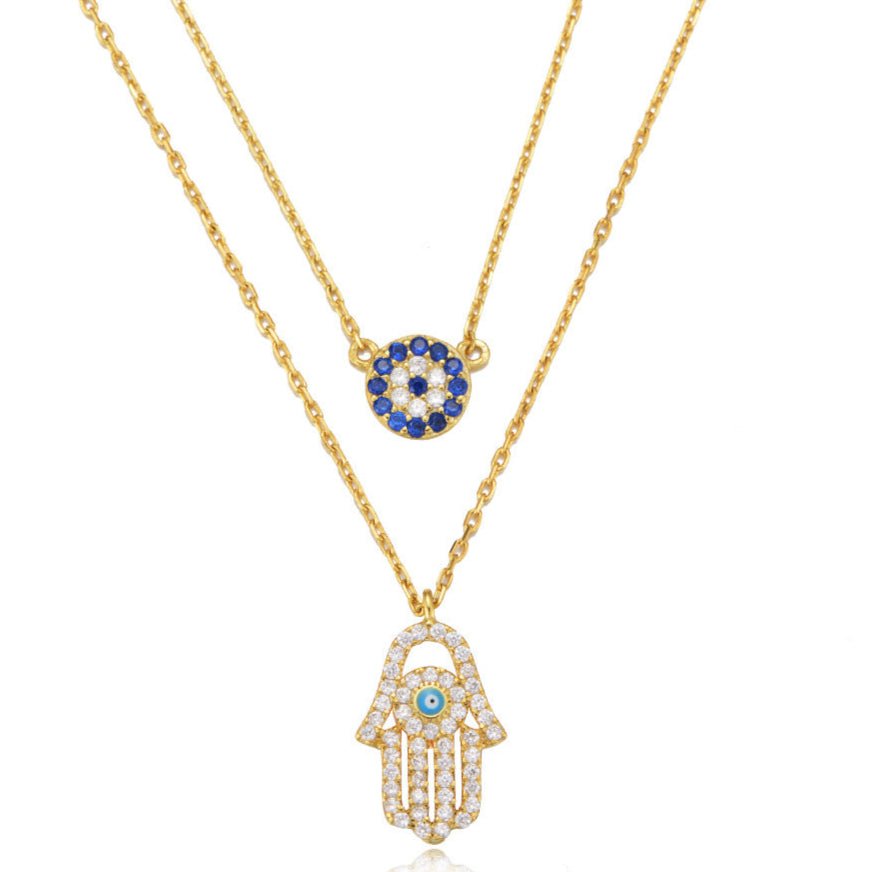 Close-up of gold layered necklace featuring blue evil eye charm and Hamsa pendant
