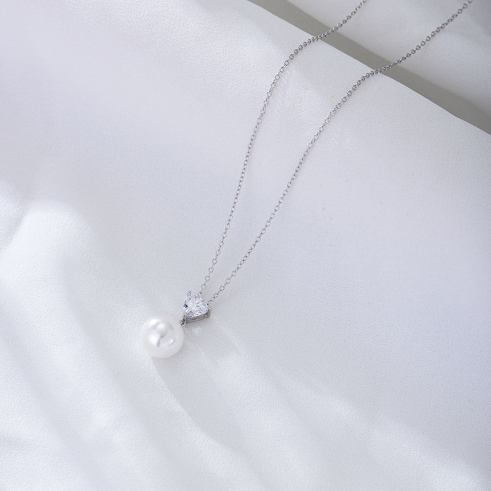	Silver S925 heart and pearl necklace with minimalist chain on satin background.
