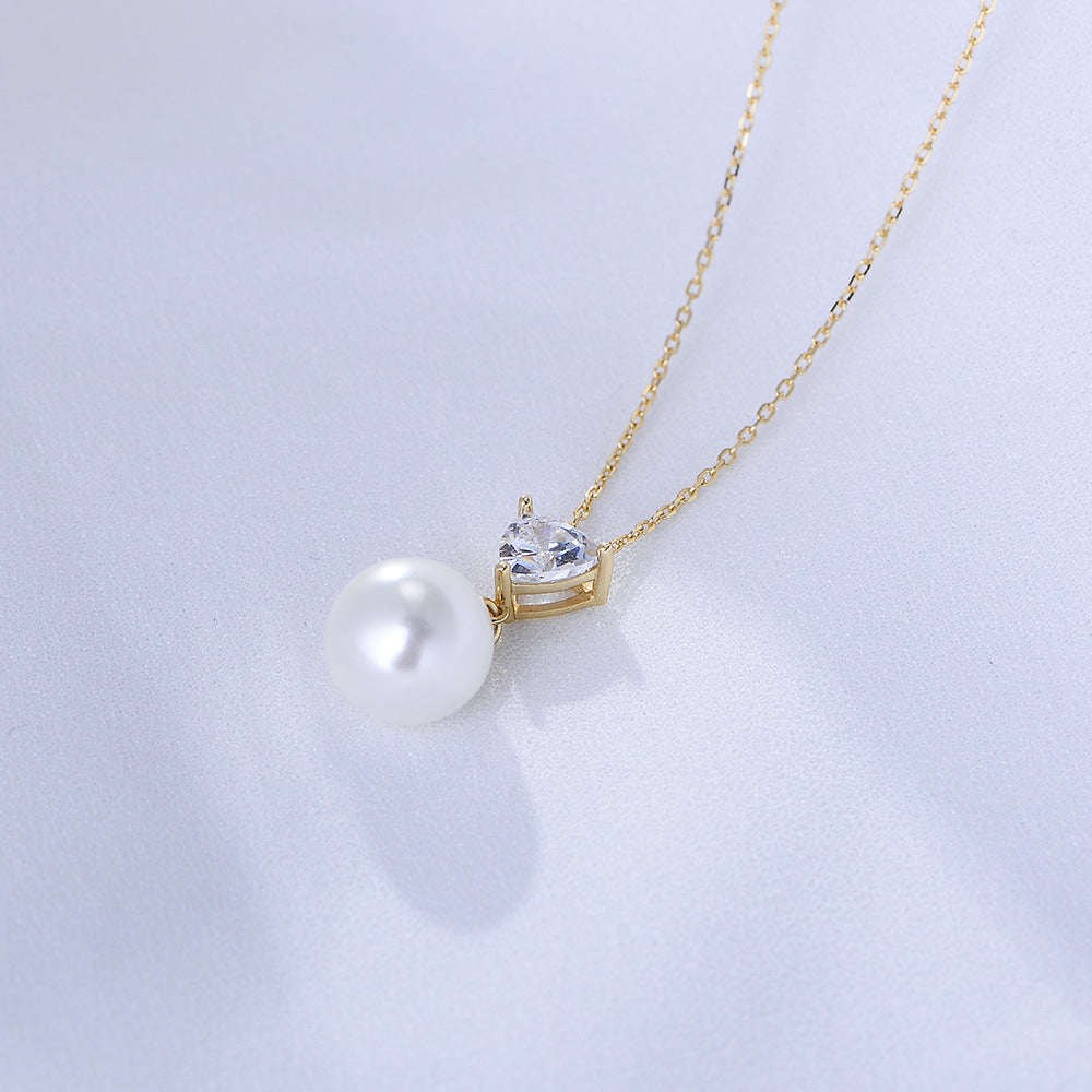 Close-up of white pearl drop necklace with heart-shaped CZ on gold chain.