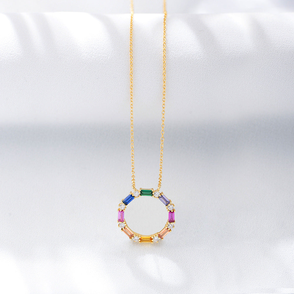Geometric rainbow CZ pendant on gold chain, shown against white textured background.