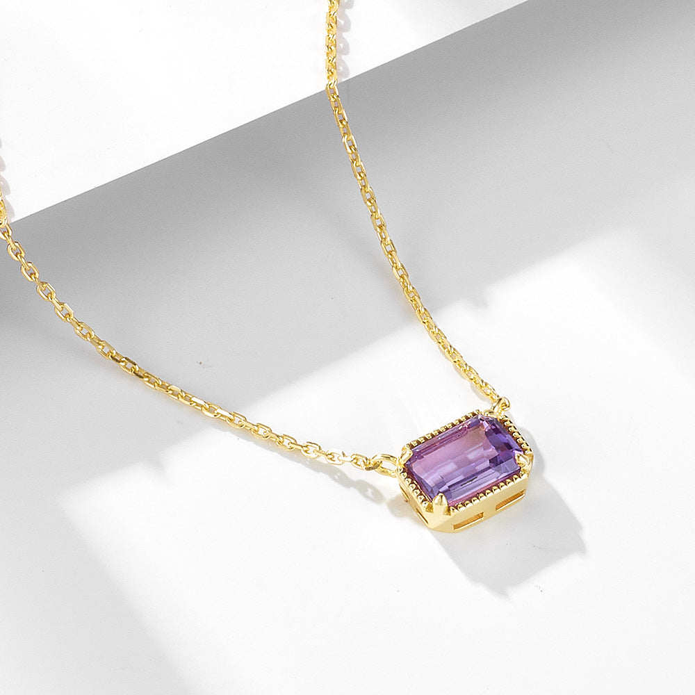Close-up of faceted amethyst pendant with gold bezel setting and textured border.