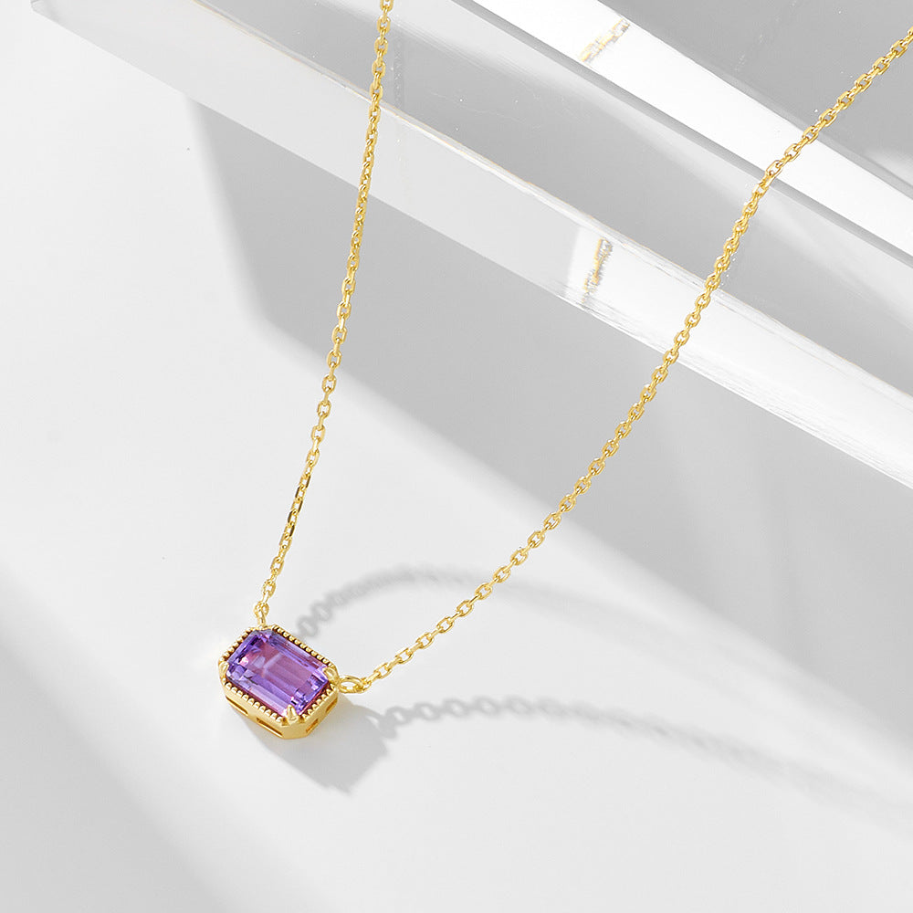 Bezel-set purple amethyst pendant on gold colored chain under soft studio lighting.